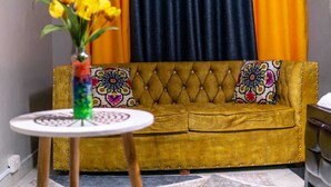 Un canapé jaune à motifs, agrémenté de coussins décoratifs, une petite table ronde sur laquelle est posé un vase de fleurs, et un mur coloré en arrière-plan.