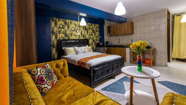 Une chambre moderne comprenant un lit, un canapé, une petite table avec un vase et un coin cuisine.