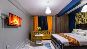 Une chambre d’hôtel avec un lit, un canapé, un téléviseur diffusant une image de cheminée et un luminaire au plafond.