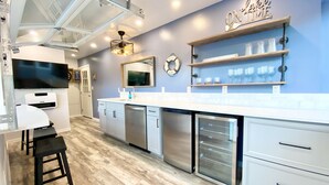 A modern kitchen with white cabinets, stainless steel appliances, and a wooden countertop. There are bar stools, a dishwasher, and a wine rack on the wall. - Beautiful cottage with lake access and bonus entertaining space! (Lakeview)