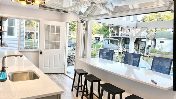 A kitchen with a large window, a sink, and bar stools. - Beautiful cottage with lake access and bonus entertaining space! (Lakeview)