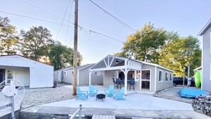 A house with a covered patio, outdoor seating, and a dock extending into a body of water. - Beautiful cottage with lake access and bonus entertaining space! (Lakeview)