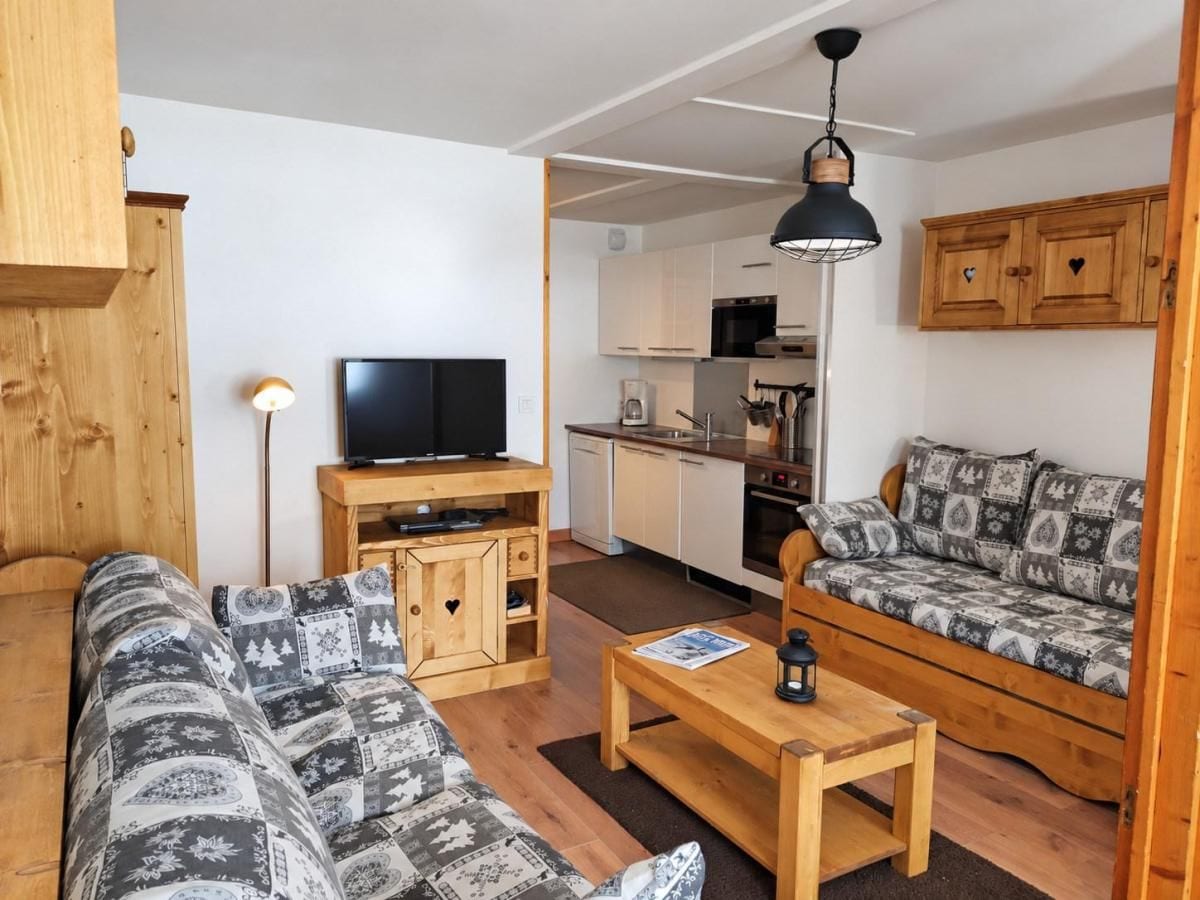 Een gezellige woonkamer met een bank, een salontafel en een televisie. Achtergrond toont een houten kast en een keukenhoek.