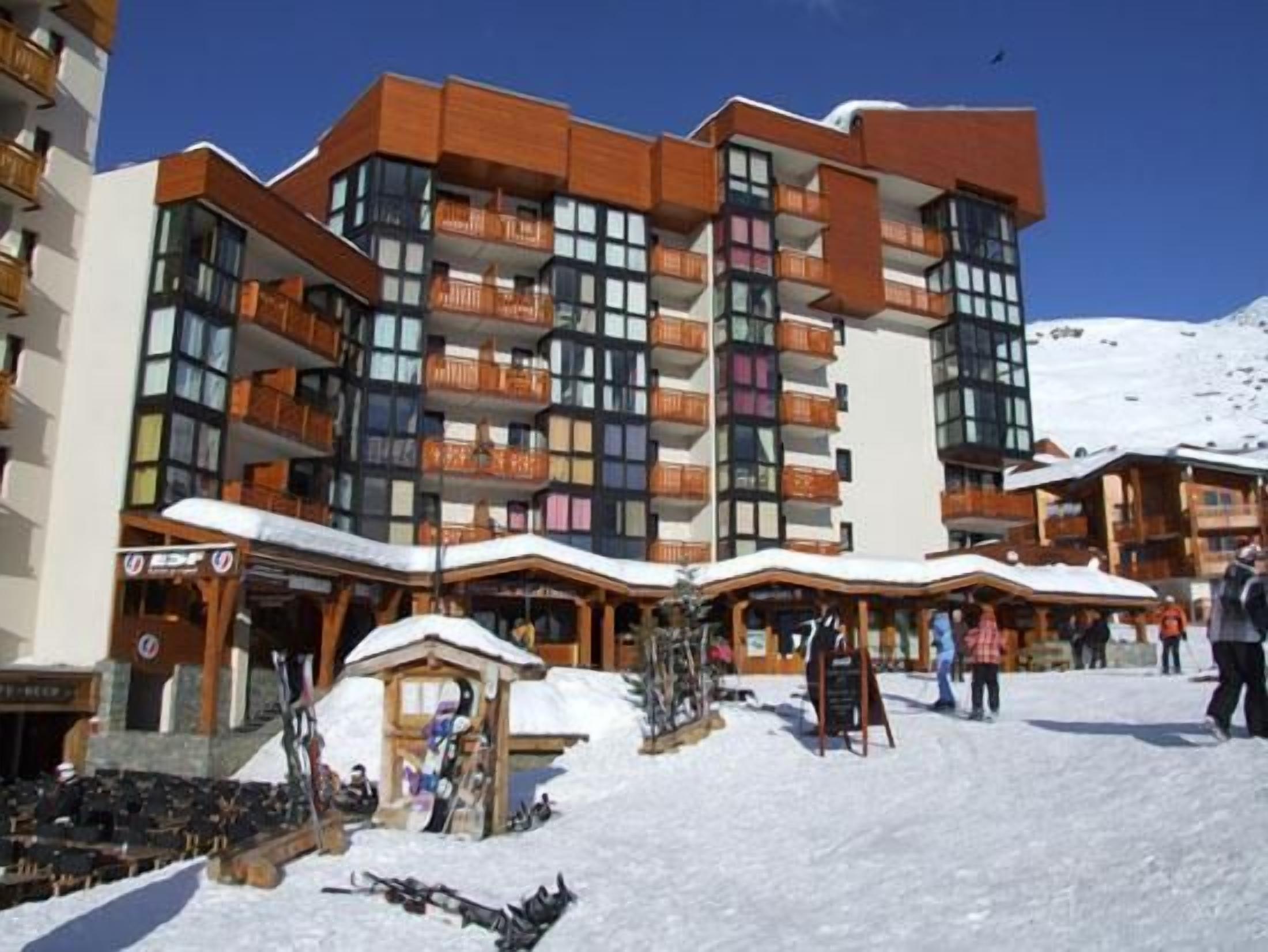 A multi-story hotel with balconies, ski equipment, and a snowy ground.
