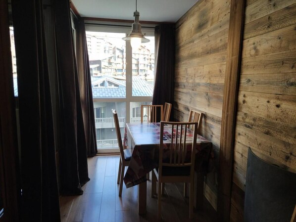 A dining area with a table and chairs, a hanging light fixture, and a view of buildings through a window.