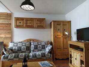 A living room with a sofa, wooden cabinets, a television, and a table with a magazine.