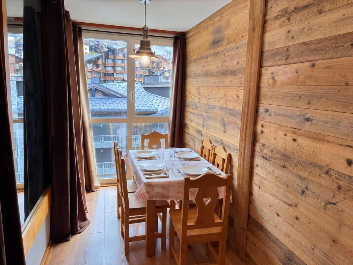 A dining area with a table set for four, wooden walls, and a view of buildings through a window.