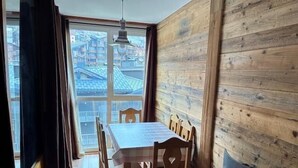 A dining area with a wooden table and chairs, a window with a view of buildings, and a wooden wall.