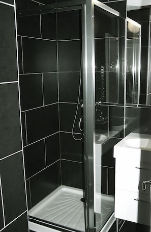 A modern bathroom with a glass-enclosed shower, black tiled walls, and a white sink.