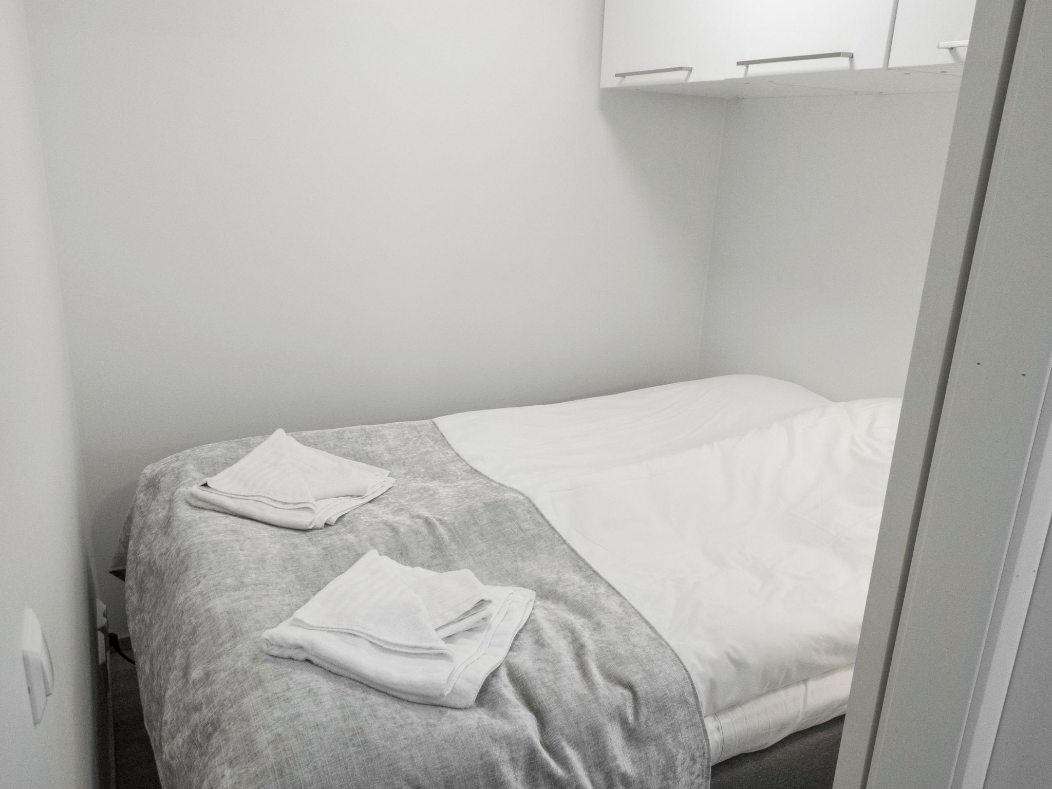 Une petite chambre avec un lit simple, une couvre-lit grise et des serviettes blanches.