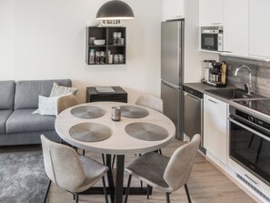A modern kitchen with a dining area, including a round table with chairs, a sofa, and a built-in oven.