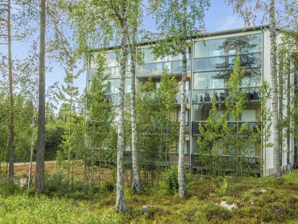 A modern building with multiple floors, surrounded by a forested area.