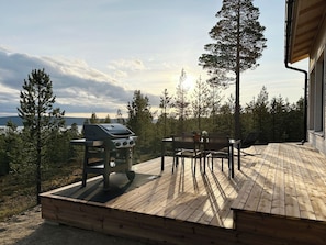 An outdoor deck with a barbecue grill, seating area, and a view of a forested landscape. - Villa horihane by Interhome (Inari)
