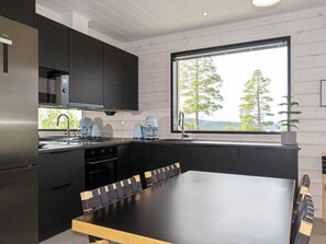 A modern kitchen with black cabinetry, a large window, and a dining area with a table and chairs. - Villa horihane by Interhome (Inari)