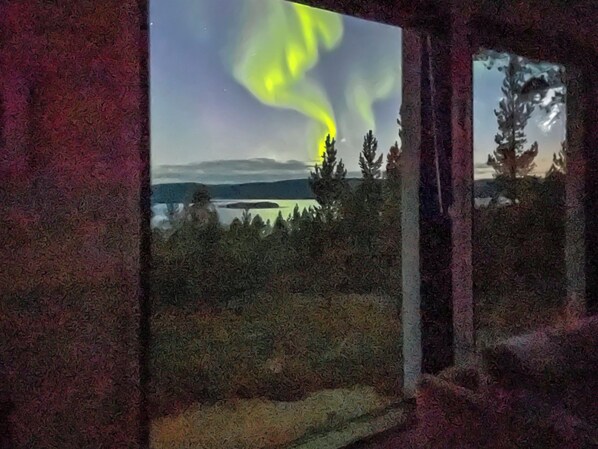 Ikkunasta avautuu näkymä metsäiseen maisemaan, jossa kauempana siintää järvi ja vuoret.