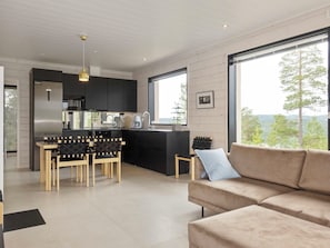 A modern kitchen with a central island, dining chairs, and a large window offering a view of trees and hills. - Villa horihane by Interhome (Inari)