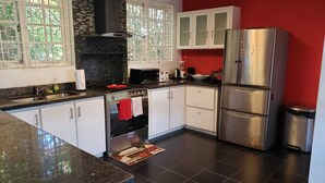 Una cocina con armarios blancos, un refrigerador de acero inoxidable, una estufa y una ventana con vista a la vegetación.