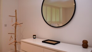 A room with a white dresser, a round mirror, a wooden coat rack, and a small candle on the dresser. - Les Dunes (Rye)