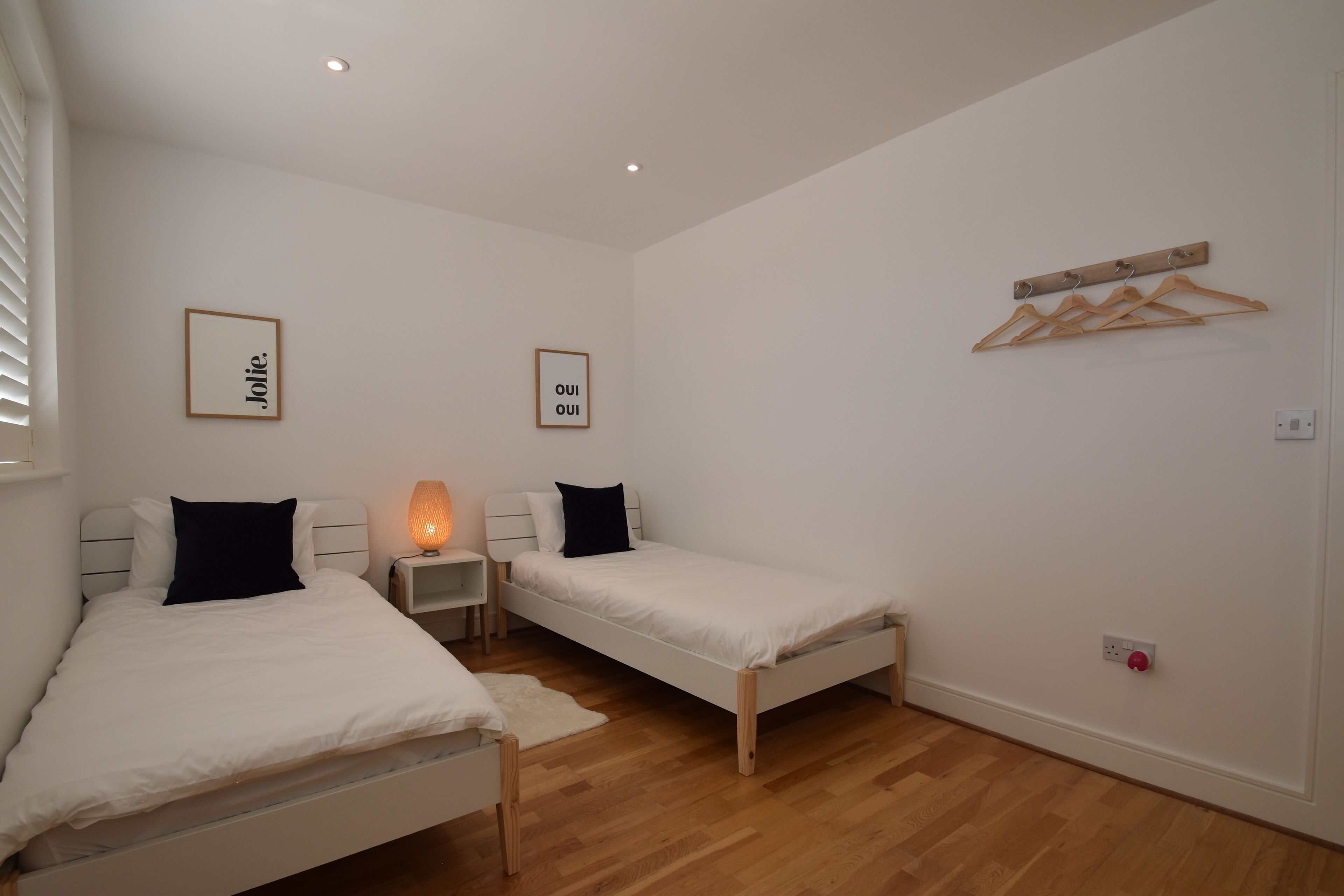 Un dormitorio con dos camas individuales, una mesita de noche con lámpara y un perchero de madera.