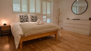 A bedroom with a wooden bed, white bedding, a bedside lamp, a dresser, and a mirror on the wall. - Les Dunes (Rye)
