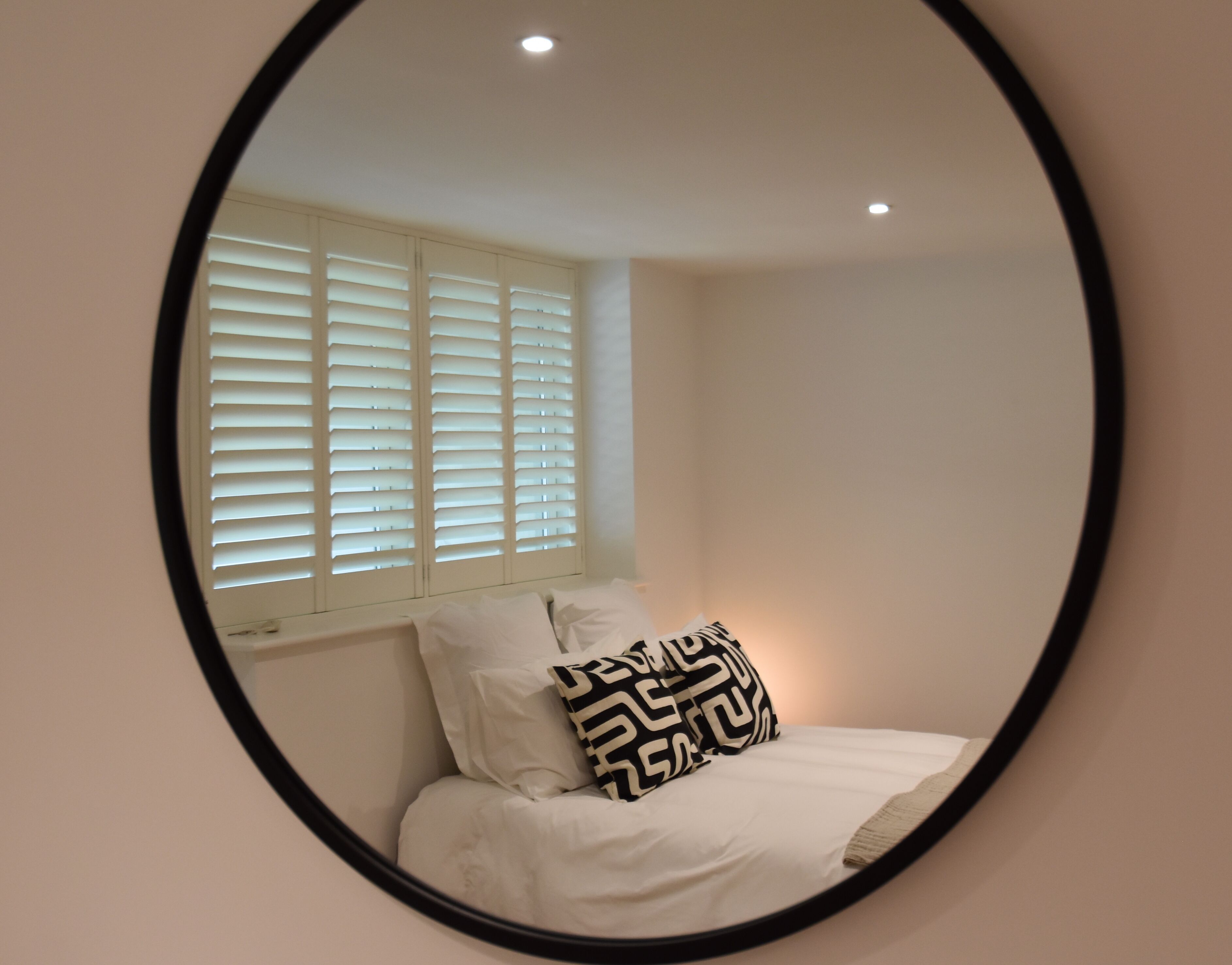 Une chambre à coucher avec un lit, du linge de lit blanc, une fenêtre avec des stores et un miroir sur le mur.