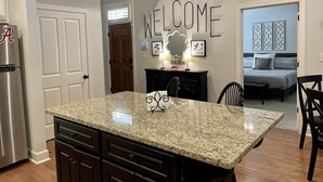 Una cocina con encimeras de granito, un refrigerador y un comedor con sillas y una mesa.