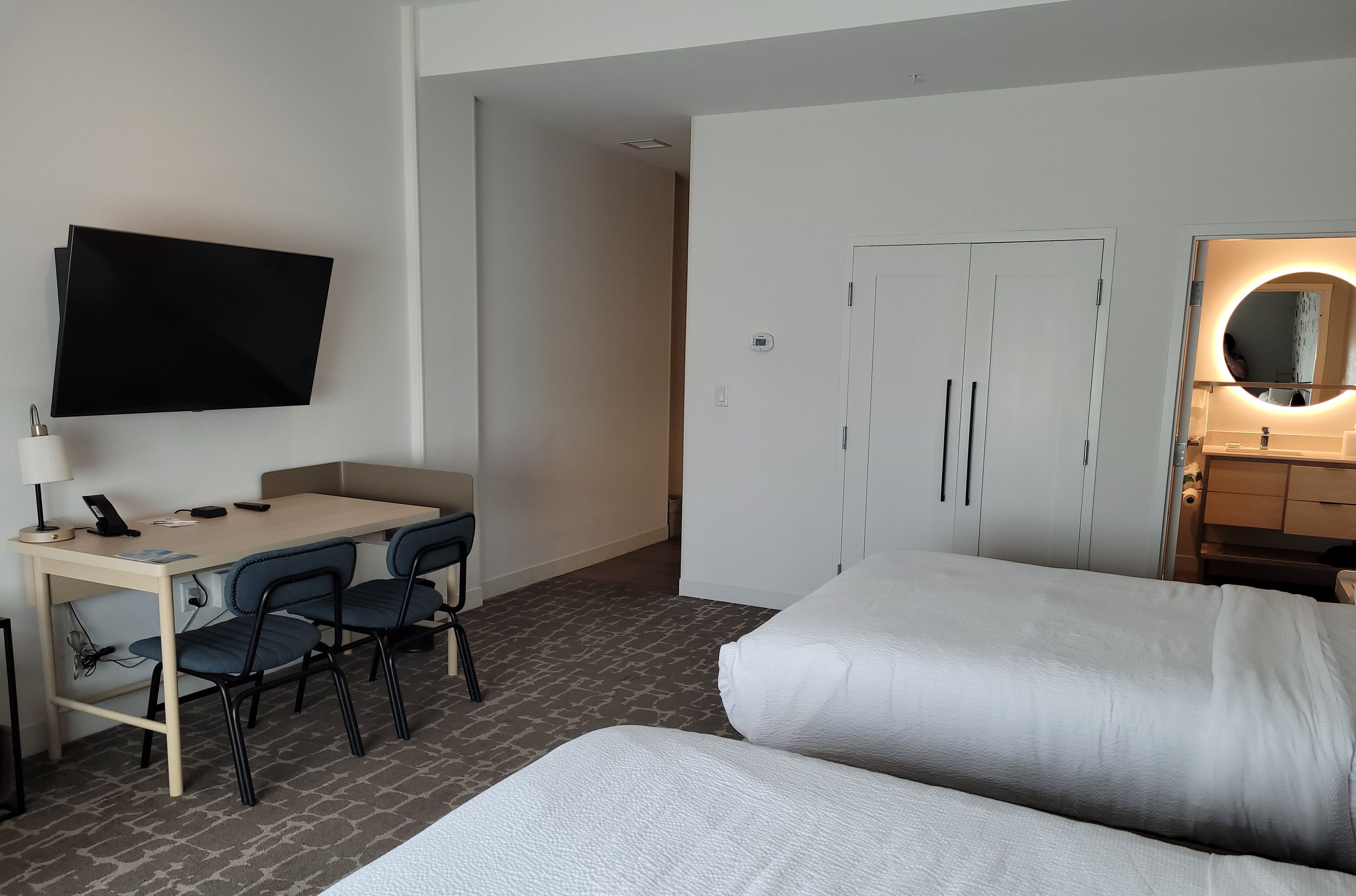 A hotel room with a bed, a desk with chairs, a TV, and a wardrobe.
