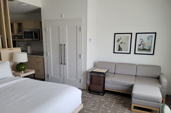 Habitación de hotel con cama, sofá, una mesita, lámpara, microondas y puerta. Hay dos cuadros en la pared.