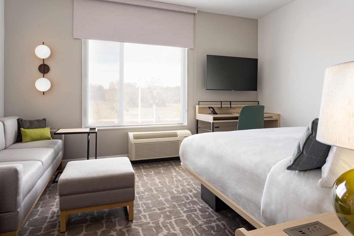 A modern hotel room with a bed, a desk, a chair, a sofa, and a TV.
