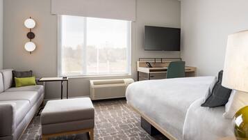 A modern hotel room with a bed, a desk, a chair, a sofa, and a TV.