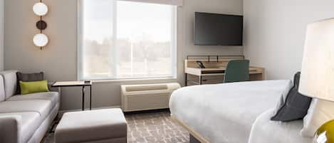 A modern hotel room with a bed, a desk, a chair, a sofa, and a TV.