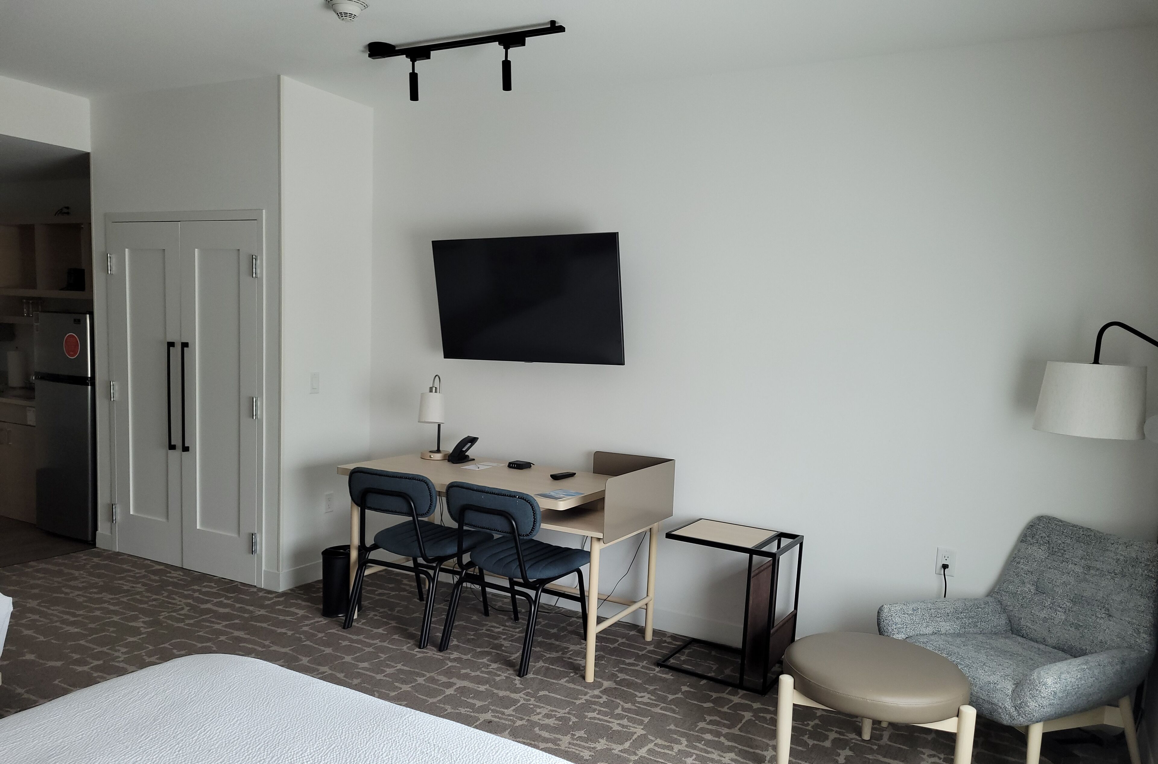 Ein modernes Hotelzimmer mit einem Bett, einem Schreibtisch mit zwei Stühlen, einem Fernseher, einer Lampe und einem kleinen Tisch.