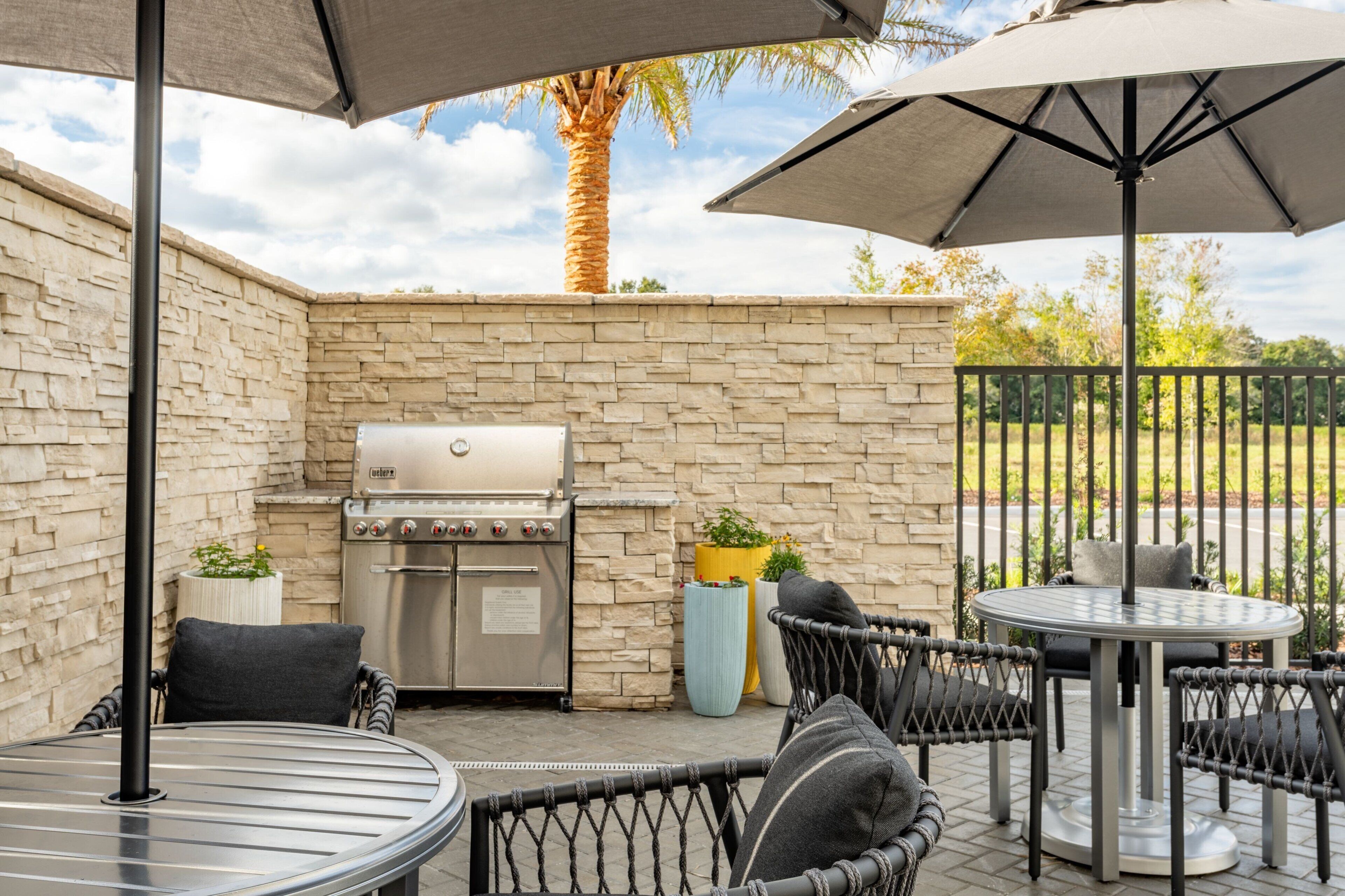 An outdoor patio with a stone wall, a grill, wicker chairs, and a round table.