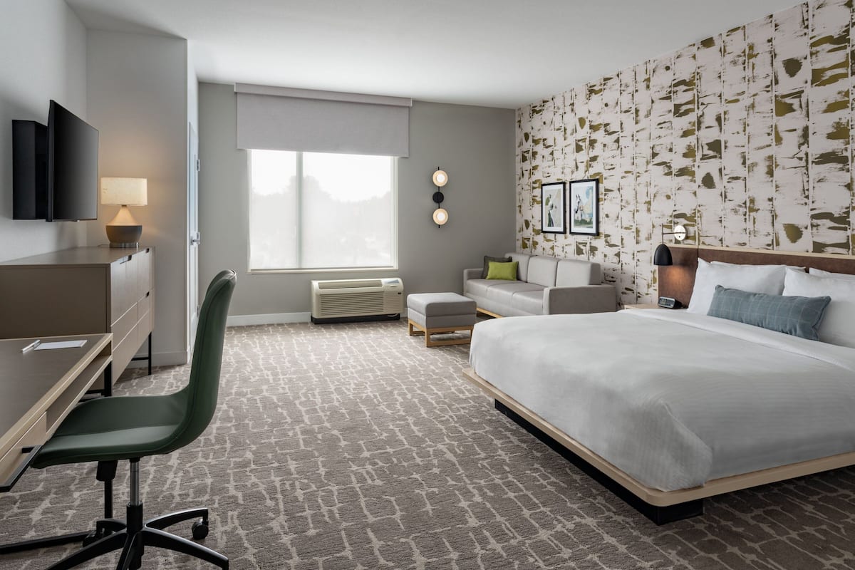 A hotel room with a bed, desk, chair, and a large window.