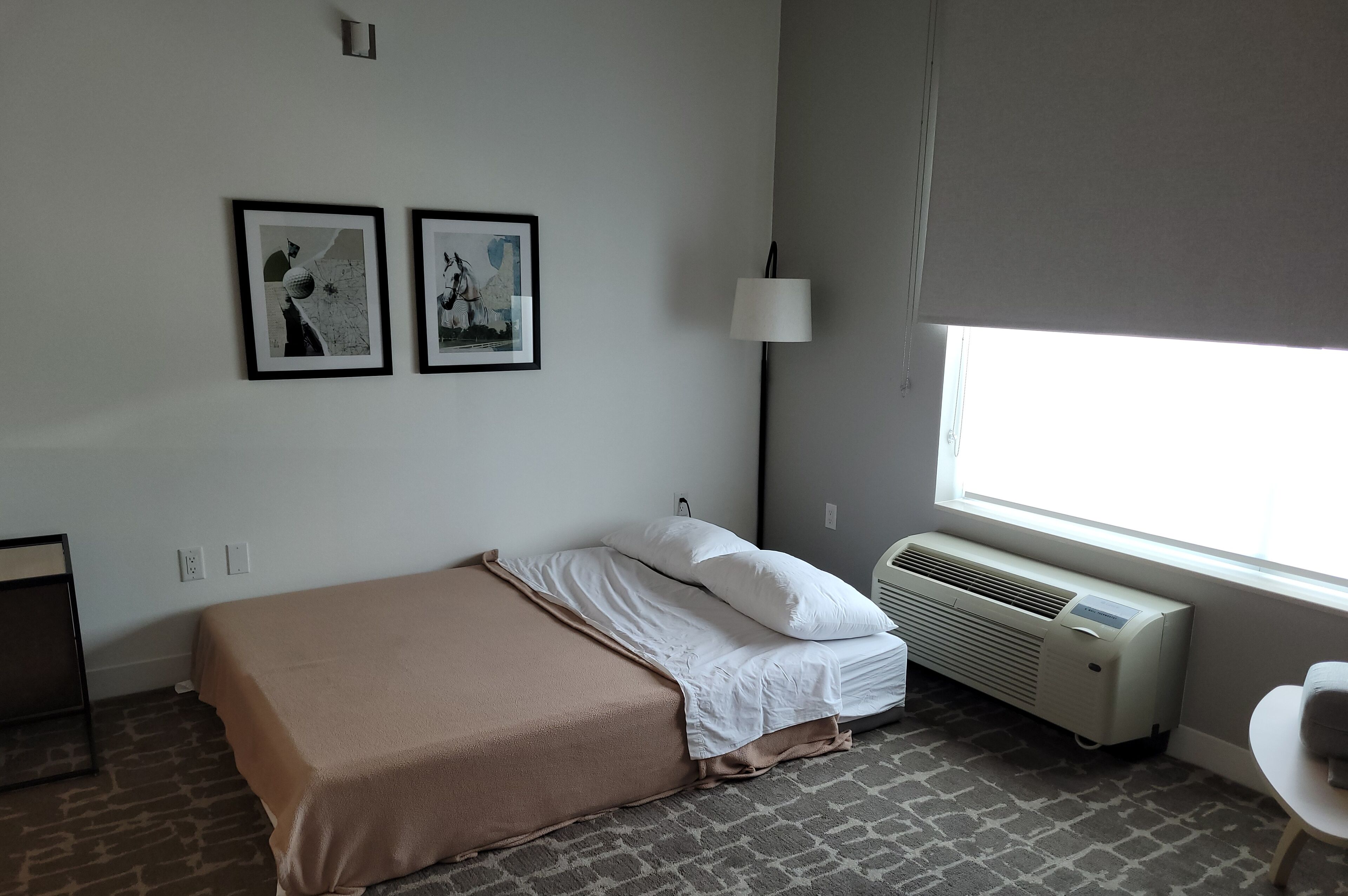 Quarto com cama, aquecedor, luminária e duas imagens emolduradas na parede.