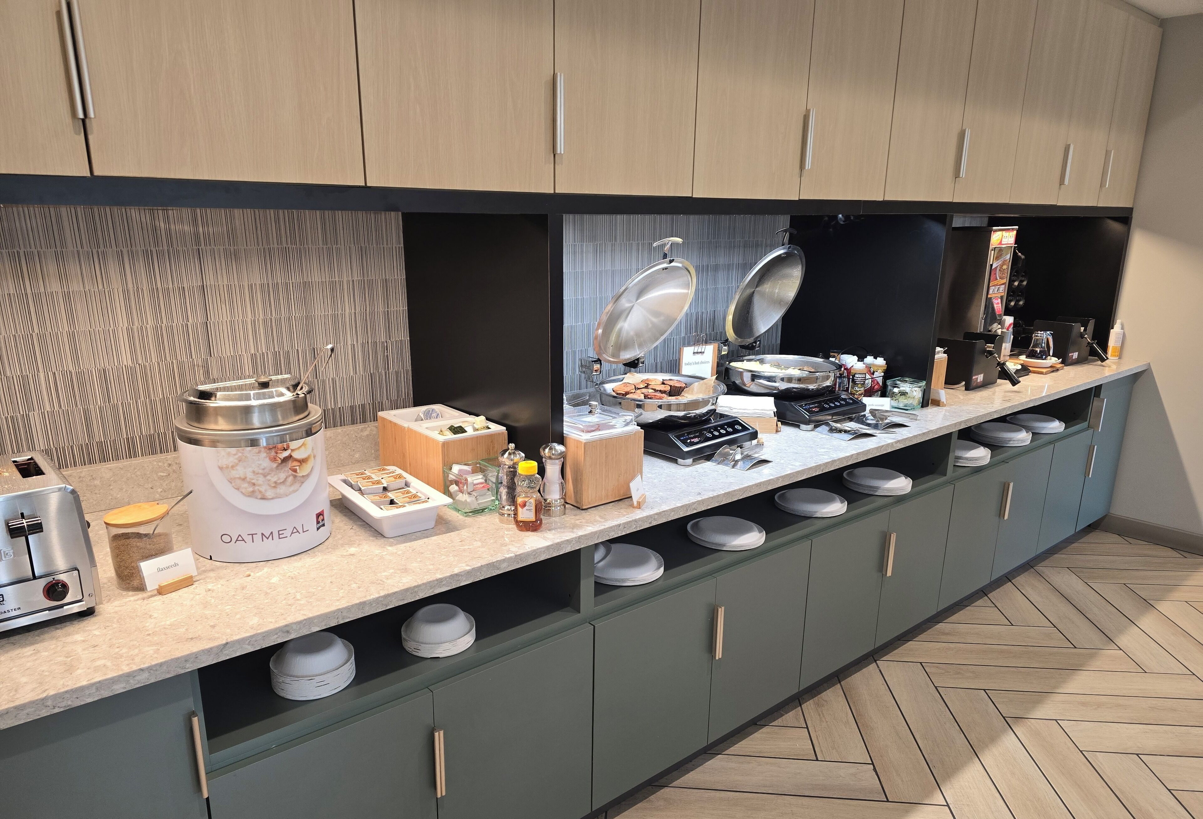 Ein reichhaltiges Buffet mit verschiedenen Speisen, darunter eine große Schüssel mit Haferflocken, eine Kaffeemaschine und mehrere Servierplatten.