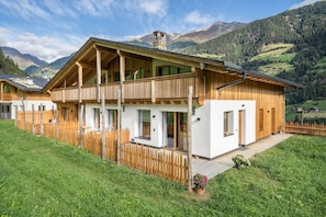 Un chalet en bois doté d’un balcon, entouré d’une clôture en bois, et situé dans un cadre montagneux.