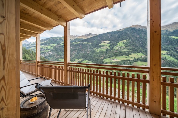 Une terrasse en bois offrant une vue sur des collines verdoyantes et des montagnes.
