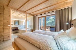 Une chambre à coucher située dans une cabane en bois, avec un grand lit, une salle de bain avec un miroir et une vue sur un paysage boisé.