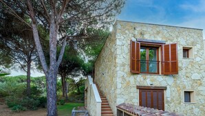 A stone building with a staircase, wooden shutters, and a tiled roof. - Vacation Home "Antonella Sul Golf" with Shared Pool, Private Terrace & Wi-Fi (Is Arenas)