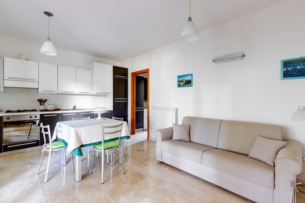 A modern kitchen with white cabinets, a dining table with chairs, a beige sofa, and a small painting on the wall.