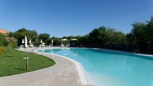 A swimming pool with a curved edge, surrounded by a paved walkway and lounge chairs. - Vacation Home "Antonella Sul Golf" with Shared Pool, Private Terrace & Wi-Fi (Is Arenas)