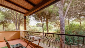 A balcony with a table, chairs, and a view of a forested area. - Vacation Home "Antonella Sul Golf" with Shared Pool, Private Terrace & Wi-Fi (Is Arenas)