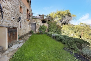 Un edificio in pietra con un cortile erboso, una porta in legno e un balcone con piante.