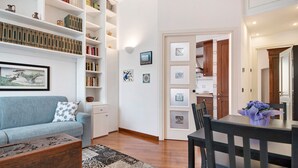 Un salon comprenant un canapé, une table basse et une table à manger. On y trouve également des étagères, une étagère murale et des tableaux encadrés.