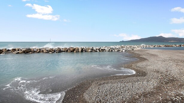 Une plage bordée d’un rivage rocheux, aux eaux calmes, avec une montagne qui se profile à l’horizon.