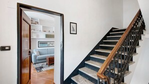 Un escalier avec une rampe en bois et des balustrades noires, menant à un espace de vie comprenant un canapé et un tapis à motifs.