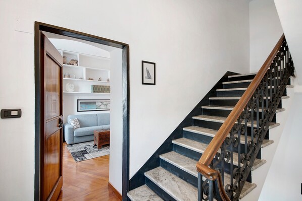 A staircase with a wooden handrail and black balusters, leading to a living area with a sofa and a patterned rug. - Apartment close to the Sea with Sea View & Wi-Fi (Chiavari)