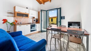 A modern kitchen with white cabinets, a dining area with a wooden table and chairs, and a blue sofa. - Holiday Home Residence Sulcis 2 with Shared Terrace & A/C (Masainas)