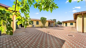 A courtyard with a tiled floor, a cactus, and yellow buildings with green shutters. - Holiday Home Residence Sulcis 2 with Shared Terrace & A/C (Masainas)